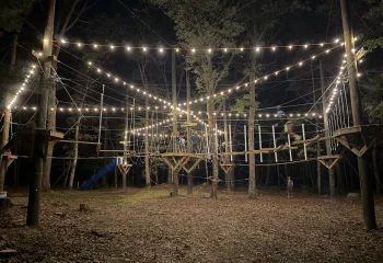 Ropes course at Camp Westwood at night, lit up with string lights.
