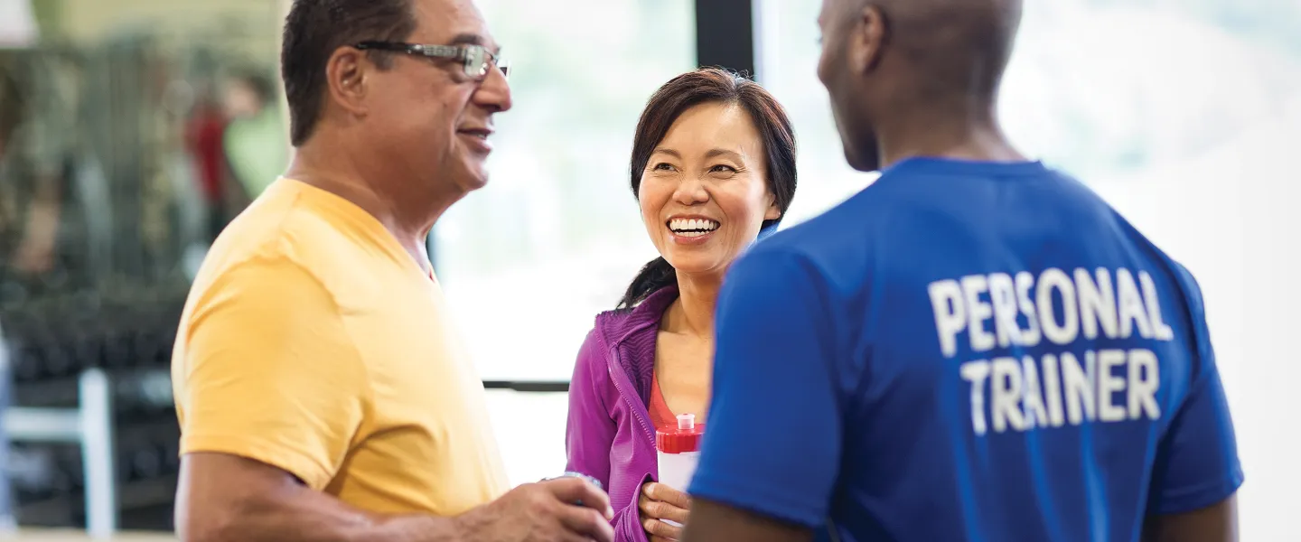 Male personal trainer talking with a man and a woman