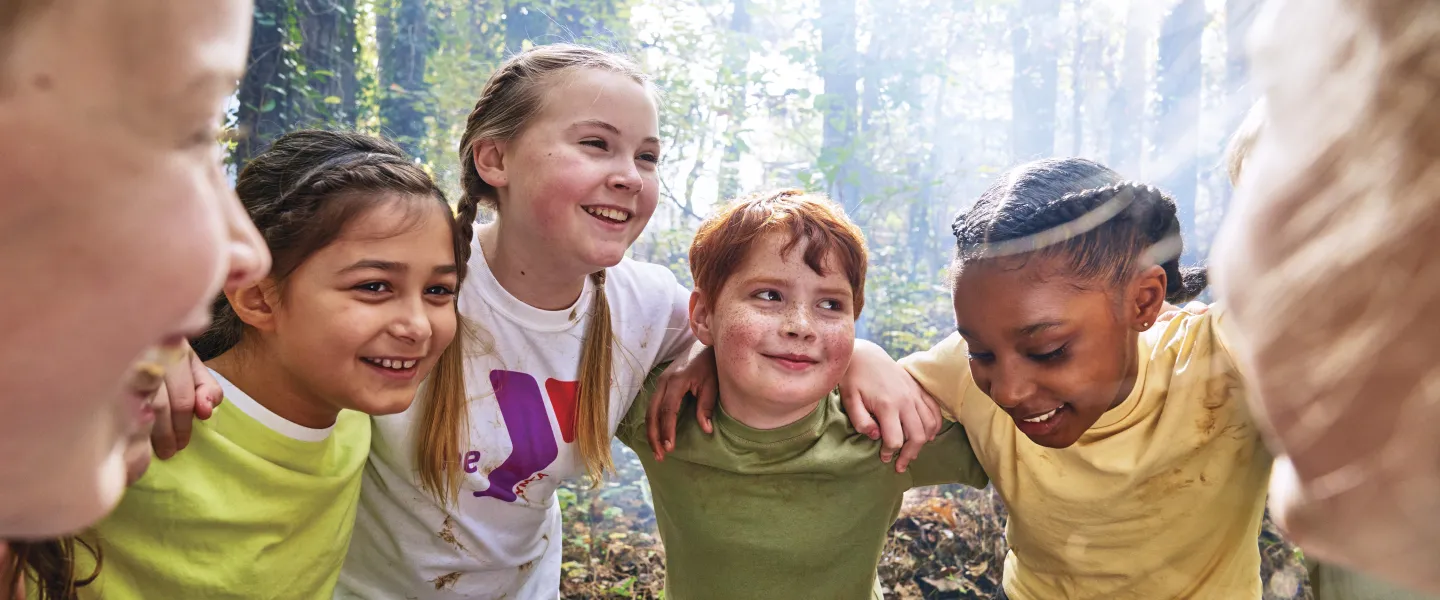 Group of kids smiling and huddling in the woods