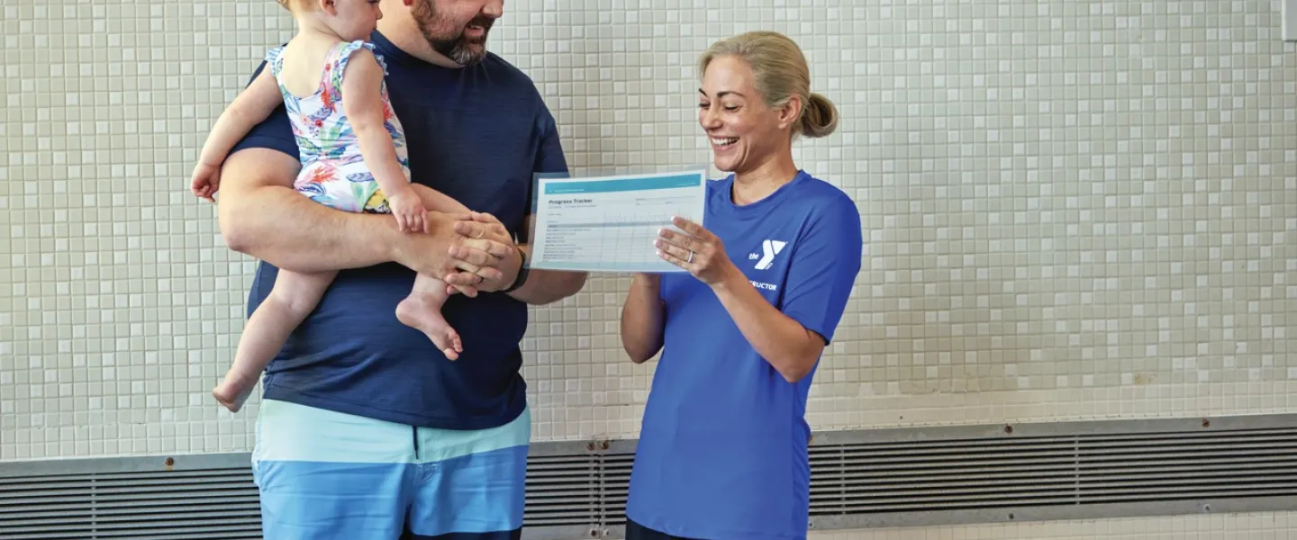 Swim instructor handing father and daughter a report card