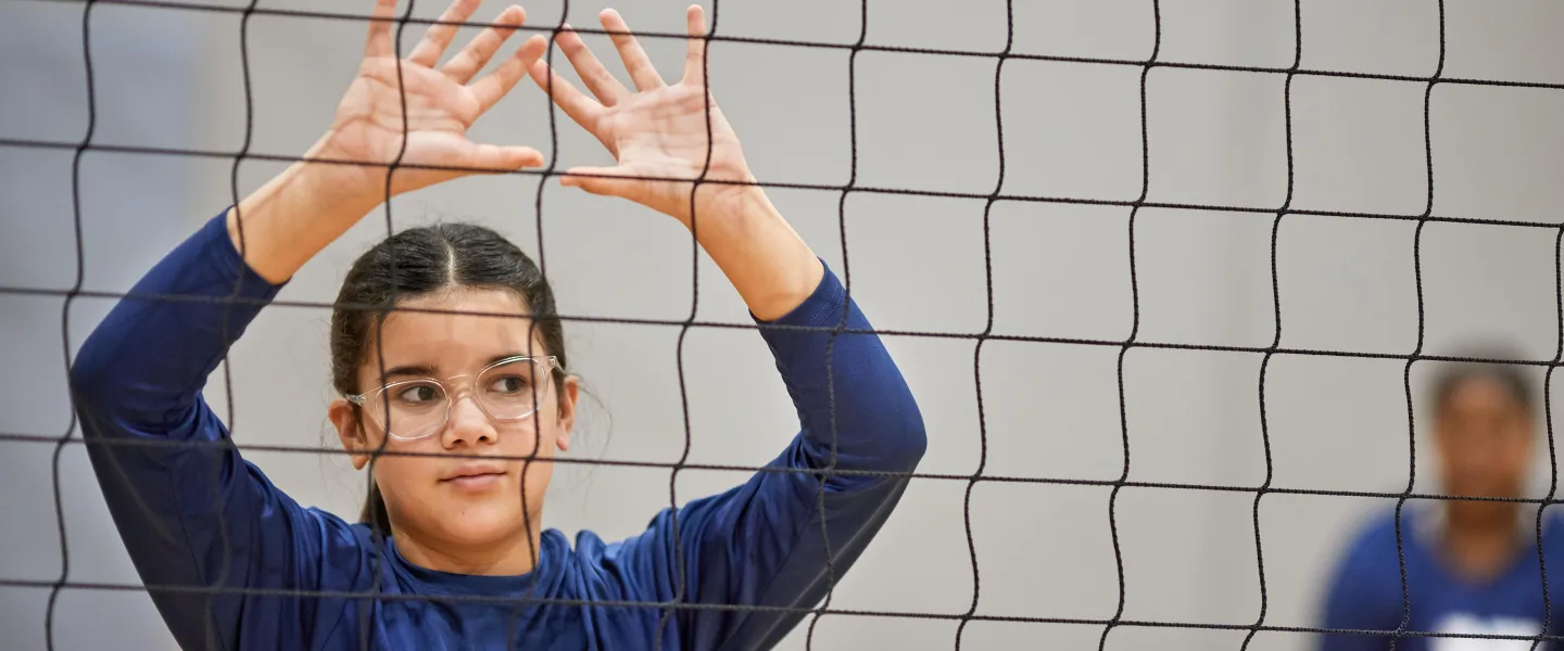 Girl with her hands up behind a volleyball net waiting for the ball