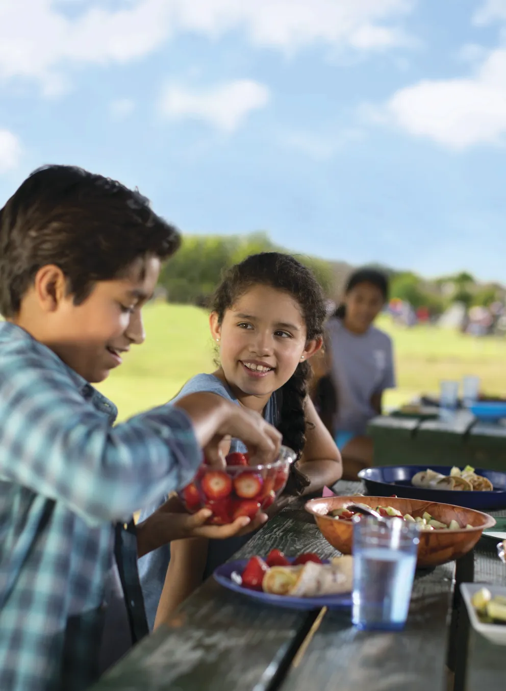 Boys and girls sitting at a picnic table outside eating food.