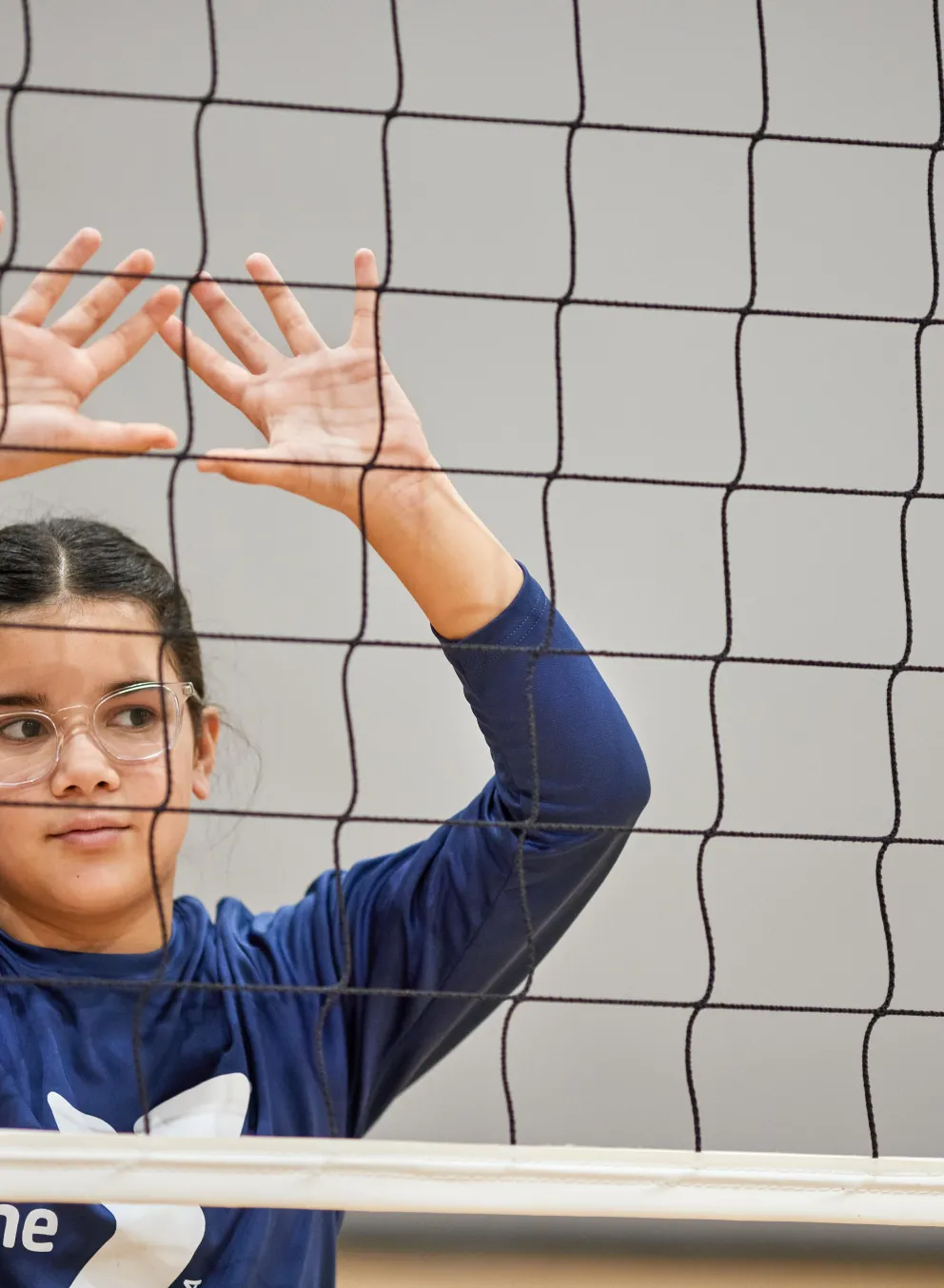 Girl with her hands up behind a volleyball net waiting for the ball