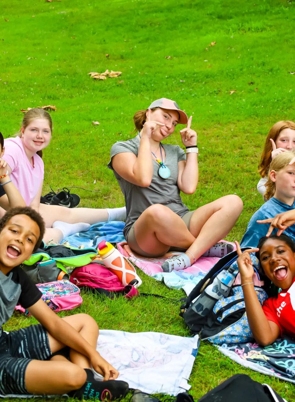 Group of campers sitting on towels in a circle in the grass.