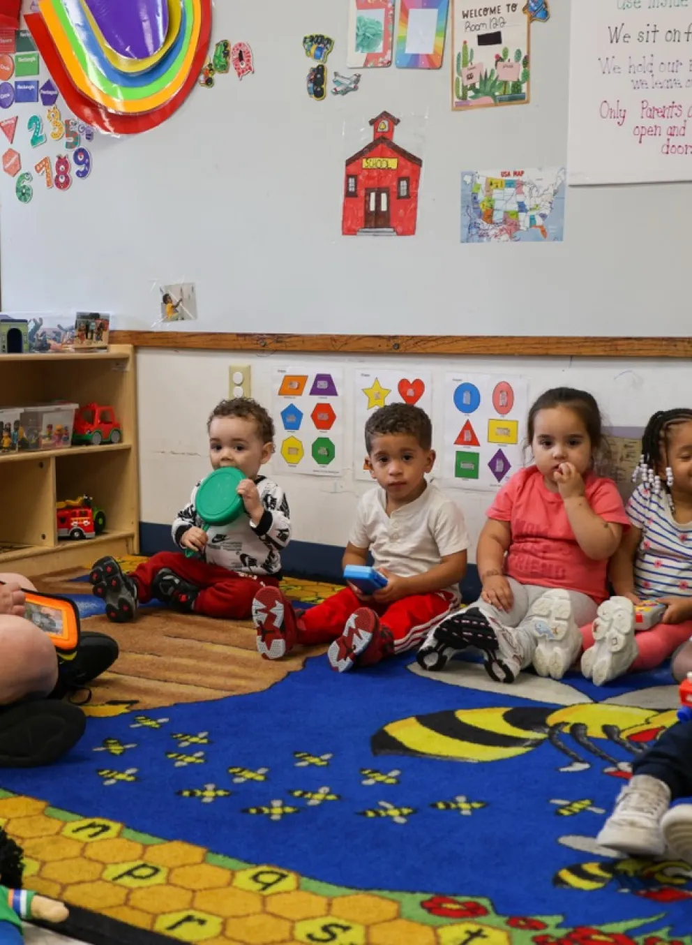 Group of six toddlers sitting on a rug infront of their teacher.