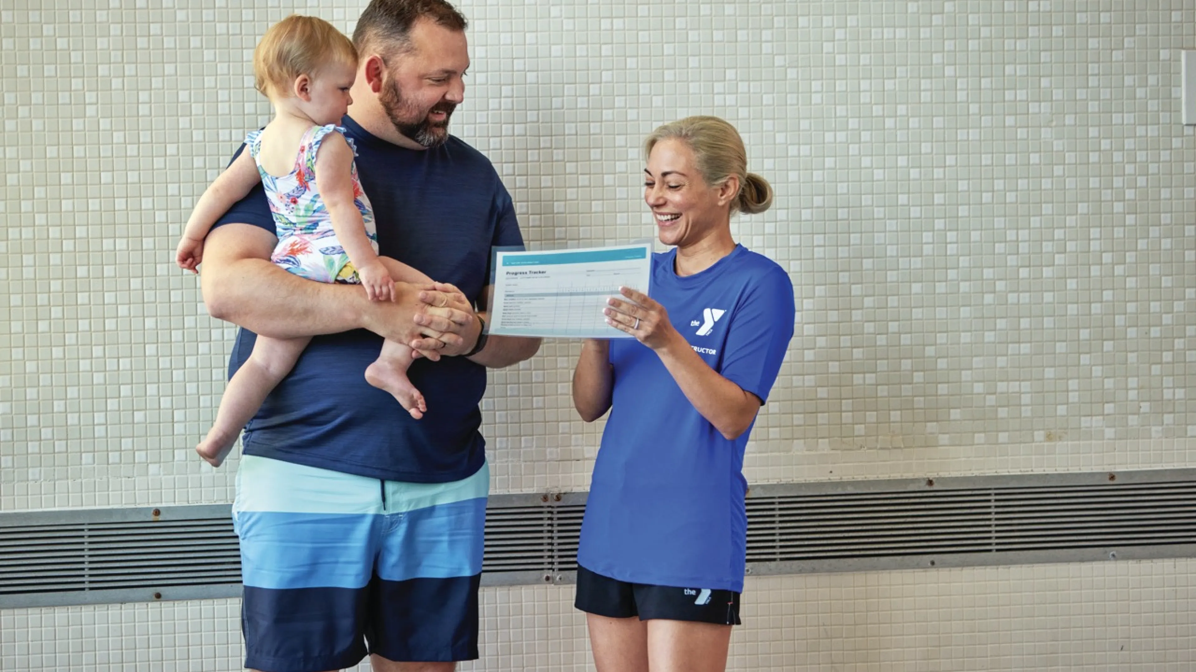 Swim instructor handing father and daughter a report card