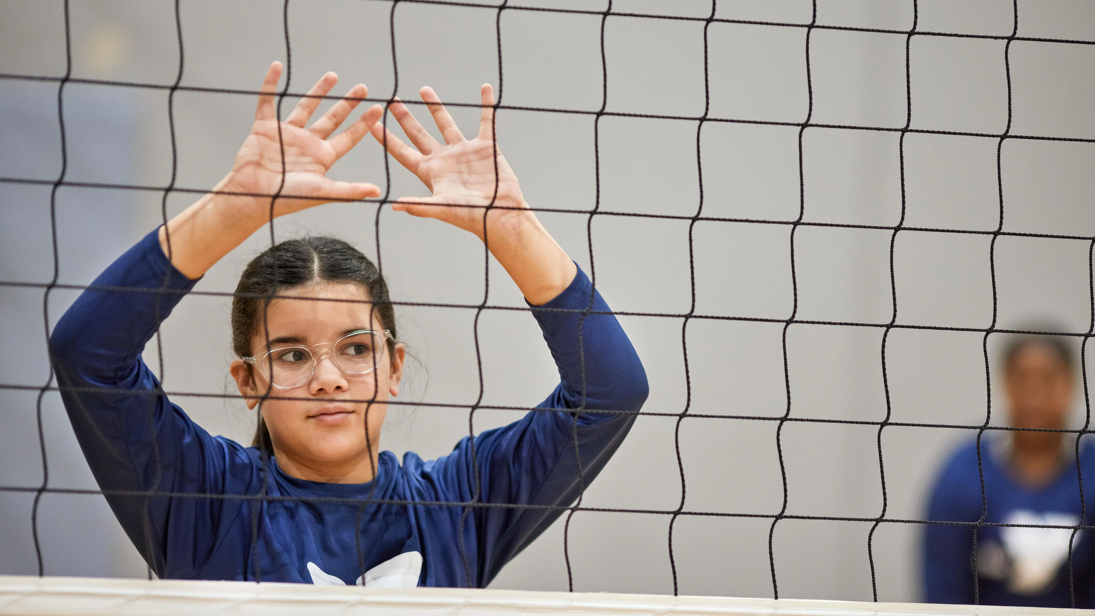 Girl with her hands up behind a volleyball net waiting for the ball