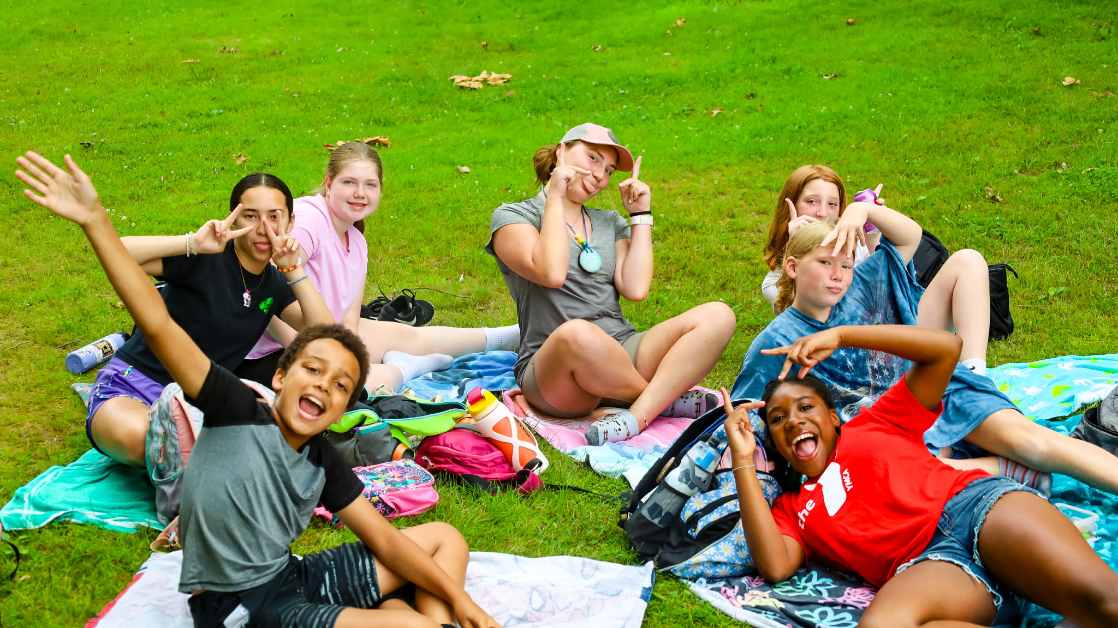 Group of campers sitting on towels in a circle in the grass.