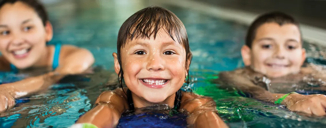 Three kids holding kickboards with swimming in an indoor pool