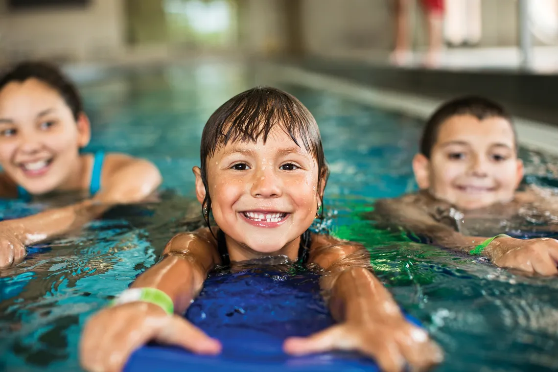 Three kids holding kickboards with swimming in an indoor pool