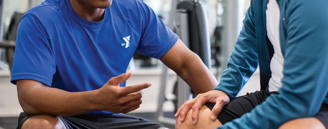 Male trainer sitting with male client holding a weight