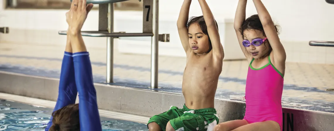 Instructor demonstrating to kids the diving position in a pool