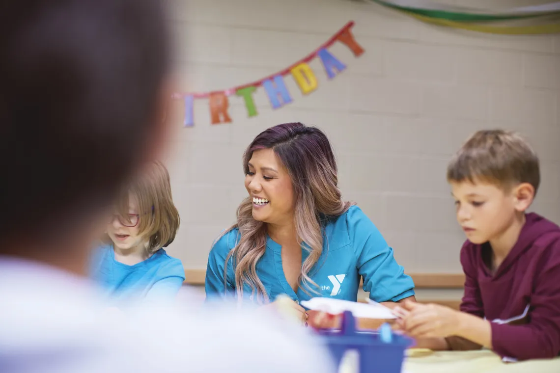 Staff sitting at table with kids with a "Happy Birthday" banner behind her