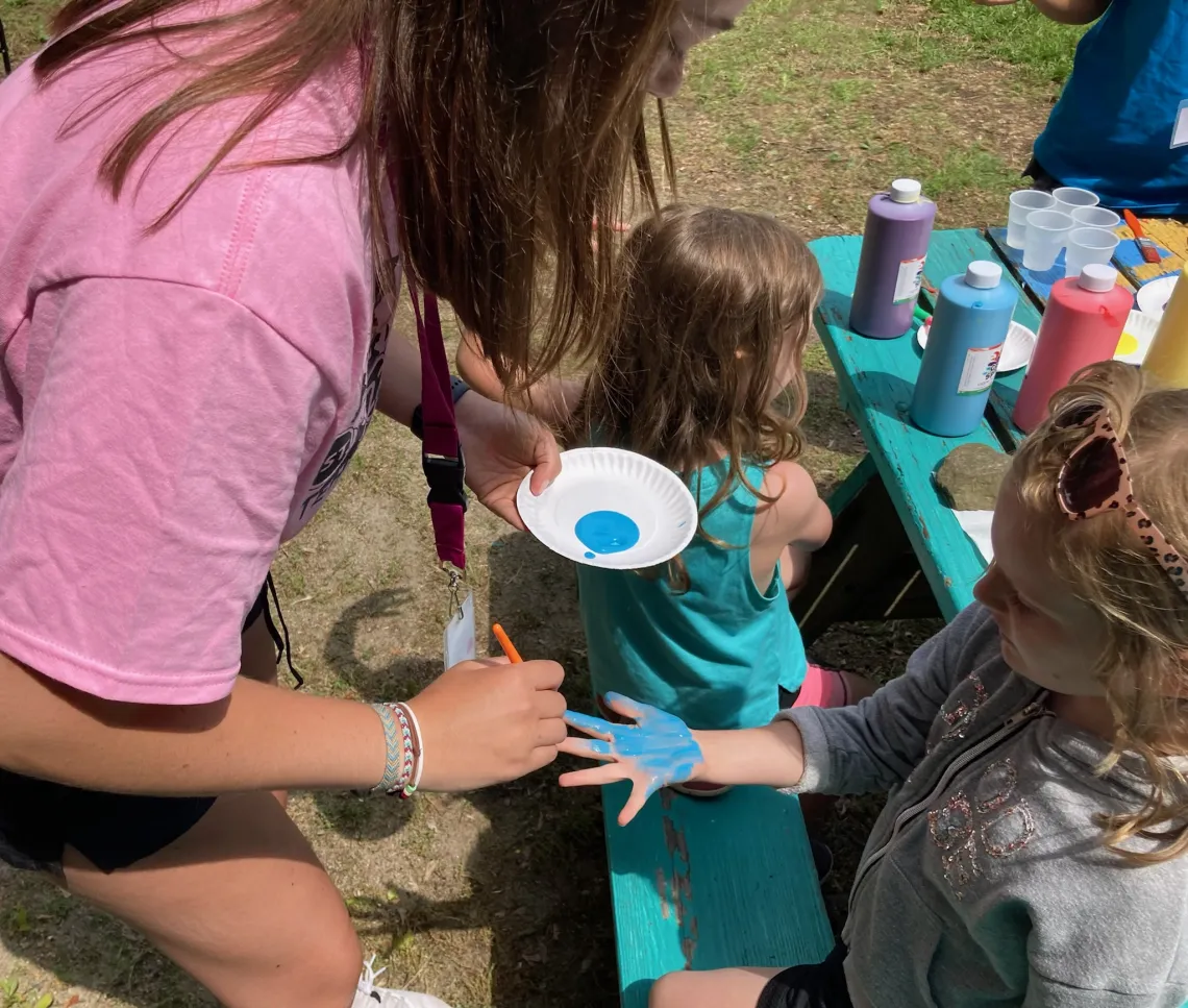 Counselor painting a child's hand blue for a craft