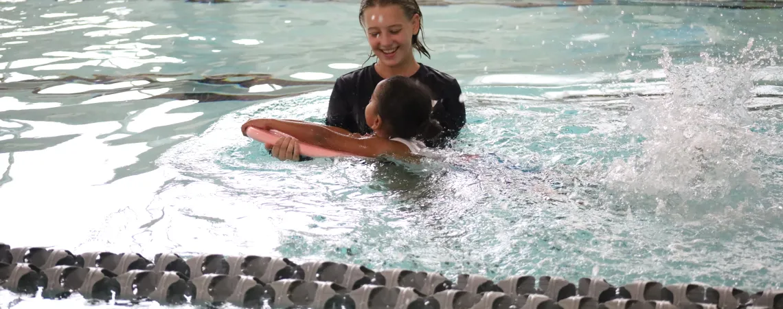 Female swim instructor teaching a girl how to swim with a kickboard