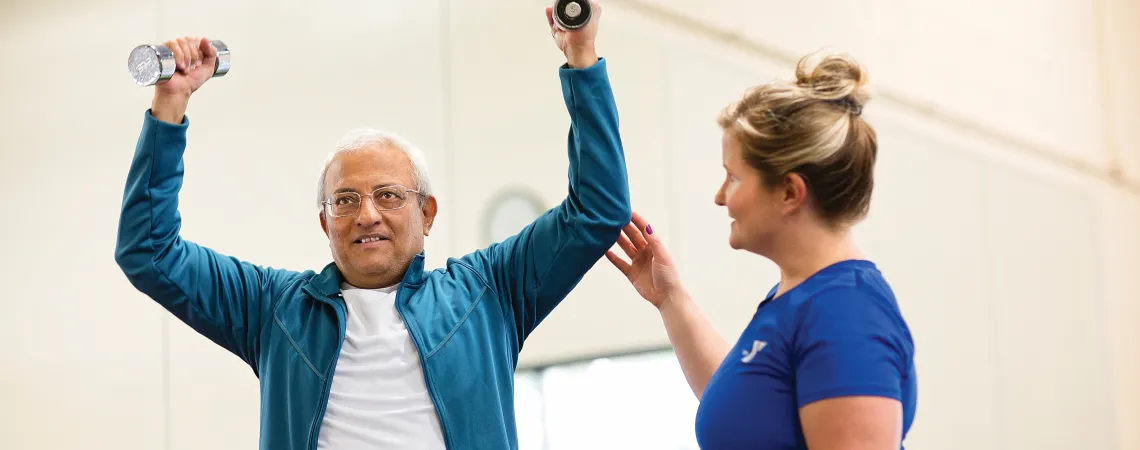 Trainer assisting man with dumbbells