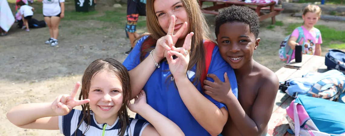 Camp Counselor smiling with campers kids on the beach at the lake