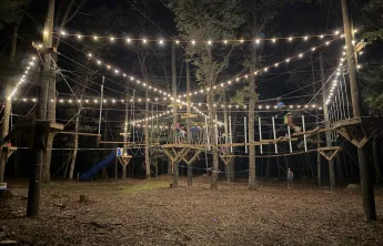 Ropes course at Camp Westwood at night, lit up with string lights.