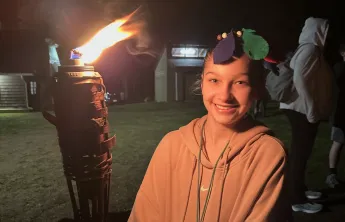 A female camper holding a tiki torch at the end of a Survivor themed Kids' Night Out.