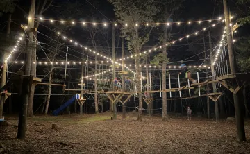 Ropes course at Camp Westwood at night, lit up with string lights.